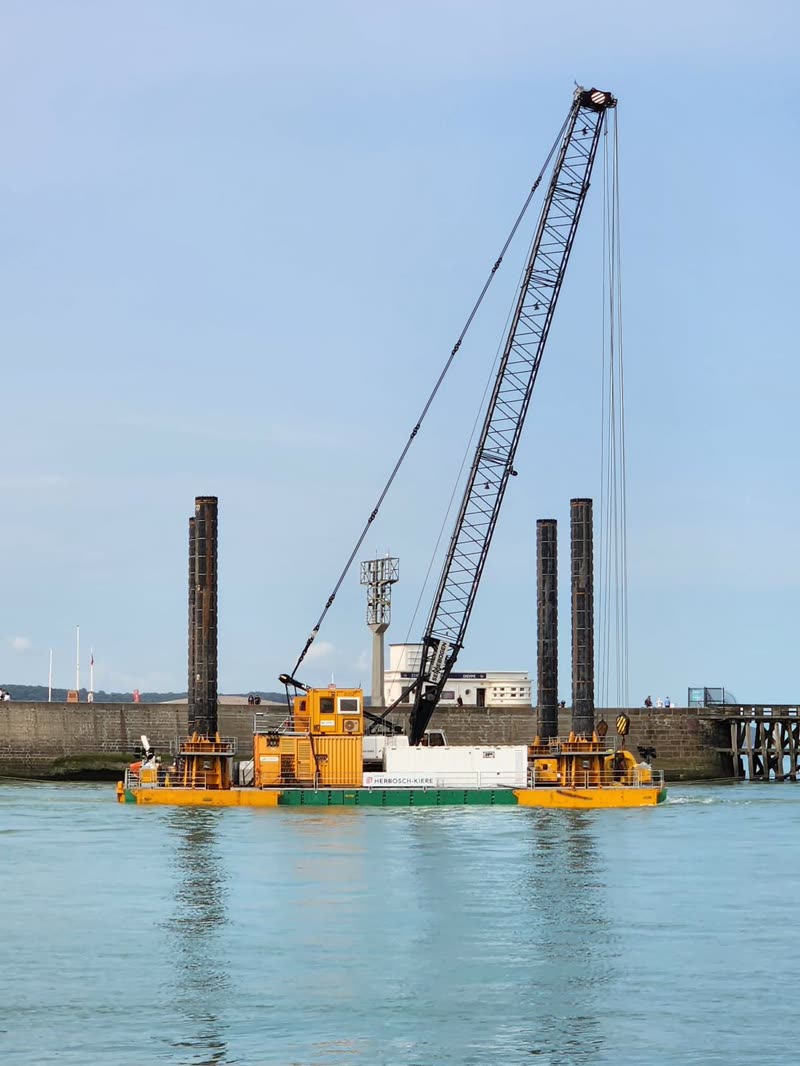 Jack-up barge with lattice crane floating beside a harbour quay