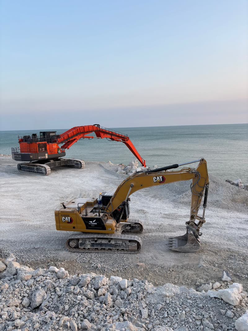 Yellow and orange excavators on a rocky coastal work platform