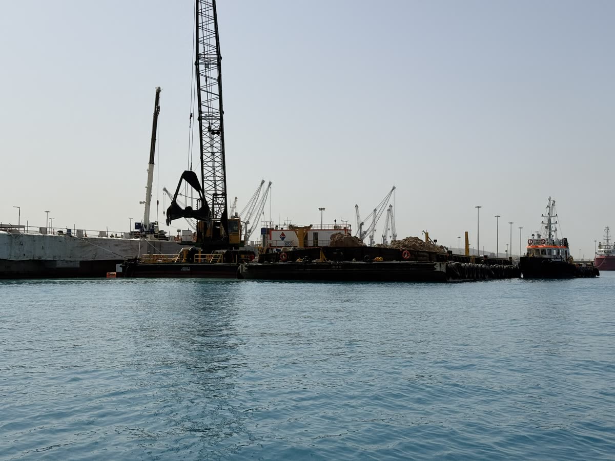 Lattice crane barge with clamshell bucket and a tug alongside