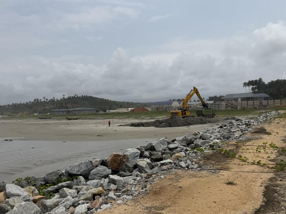 Beach excavator loading a dump truck beside a stone revetment