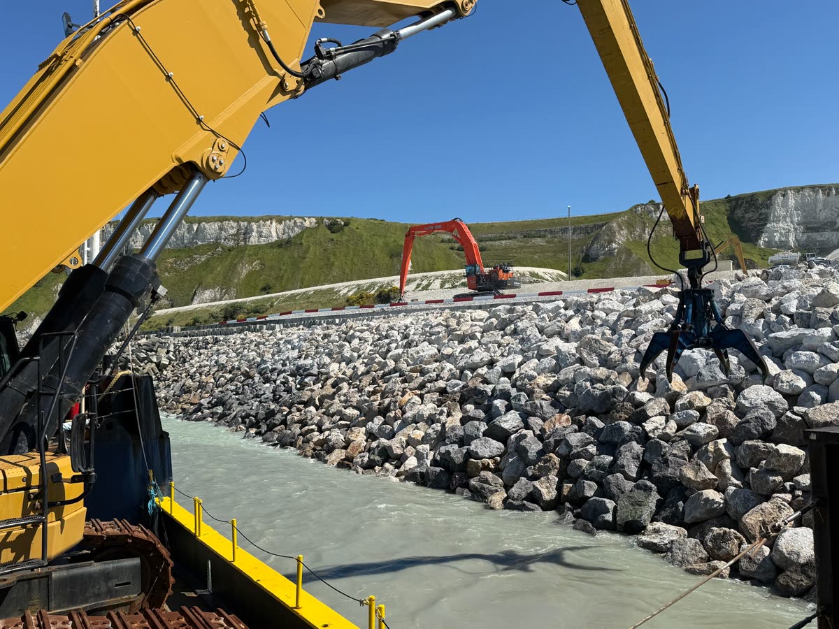 Excavators and a grapple placing rock on a riprap slope
