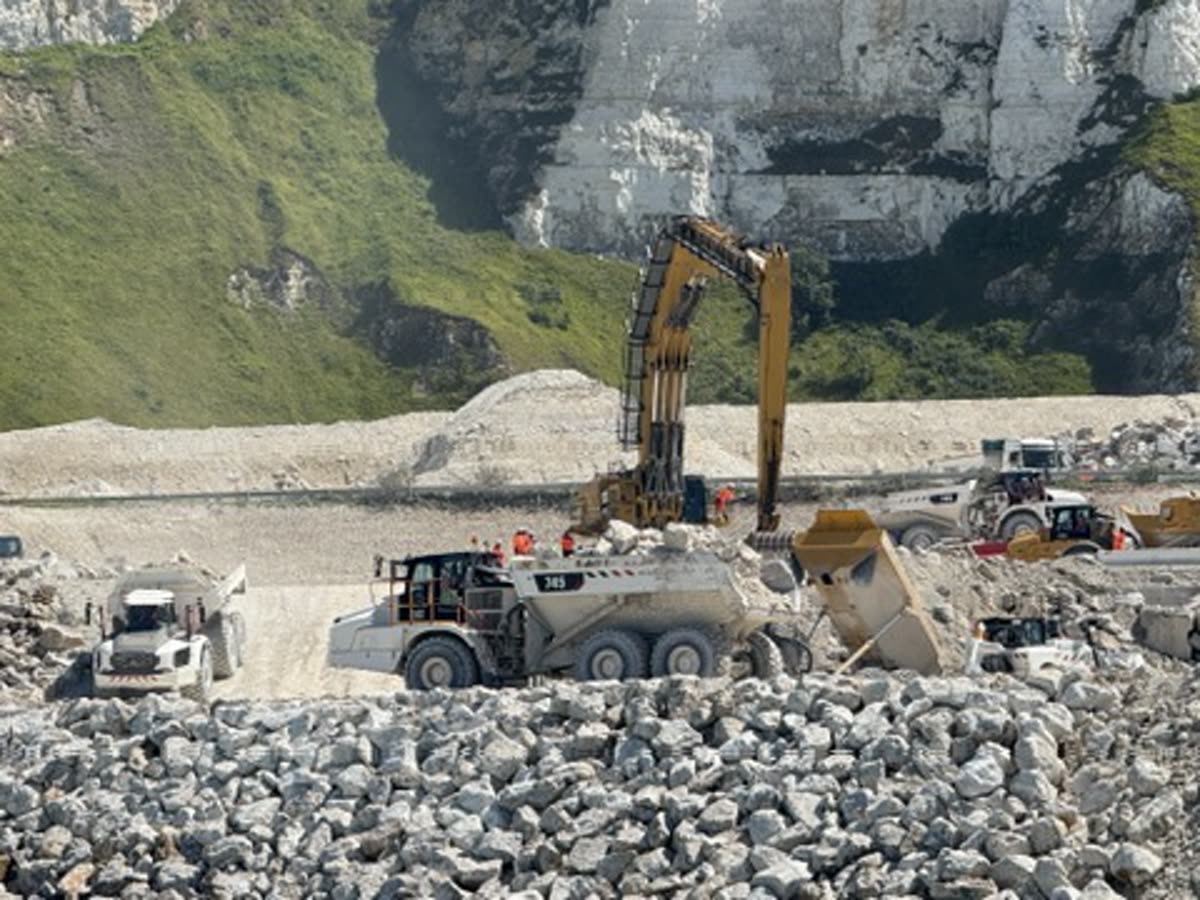 Dump trucks and excavator loading chalk fill below a cliff